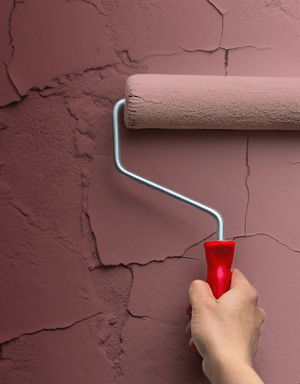 Paint roller covering a cracked wall with peeling paint