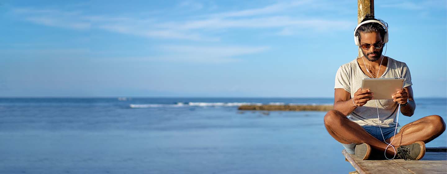 Man working remote on a beach wearing headphones and looking at tablet